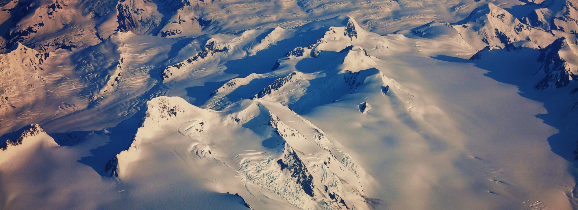 Aerial view of snow-covered mountain peaks and ridges under low sun — the kind of terrain Mount Vinson sits in