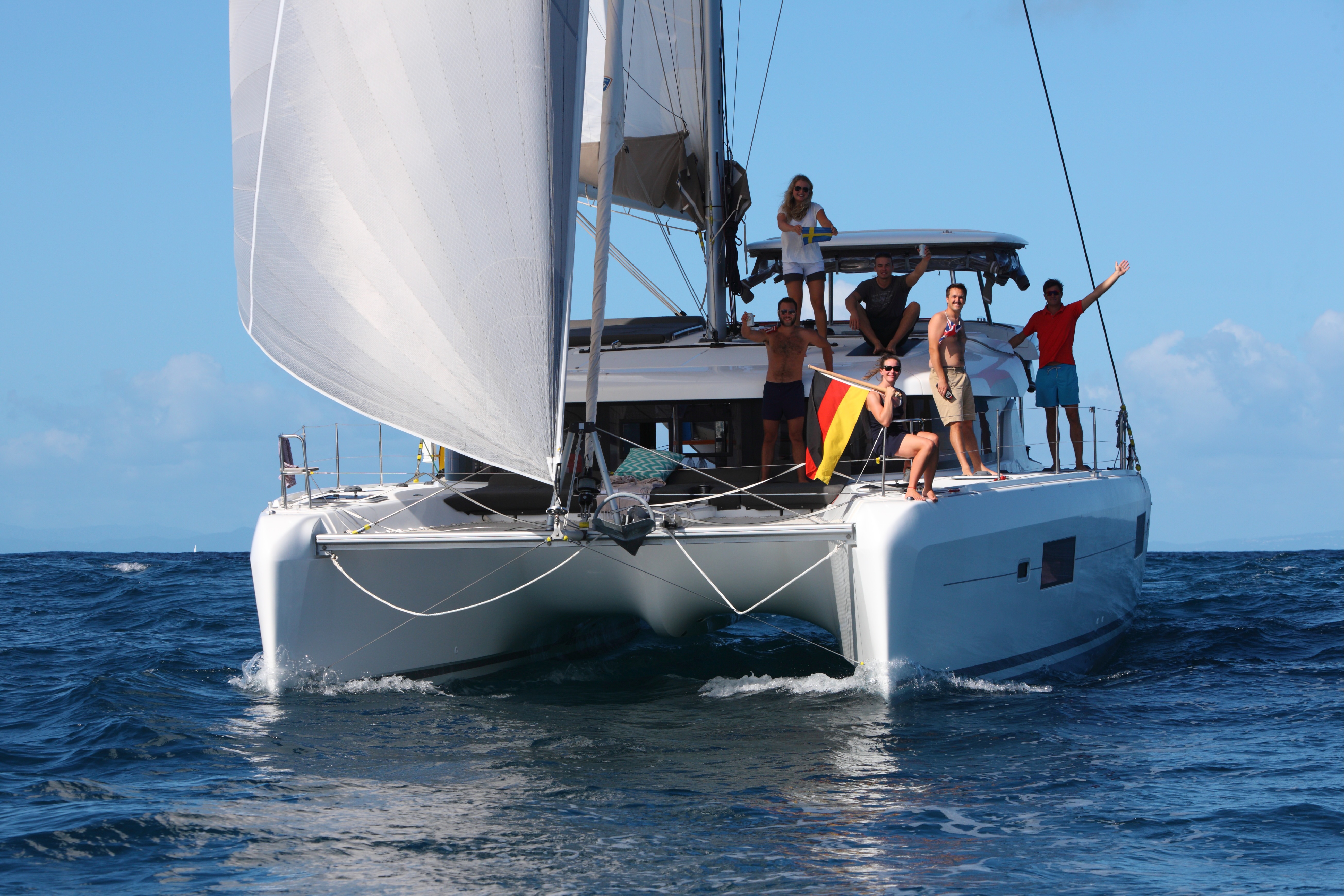 Crew of seven aboard a sailing catamaran mid-Atlantic, sails up, sun on the water